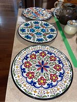 Three hand painted ceramic plates arranged in a line showing different floral and geometric designs, no visible chips or cracks.