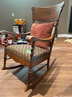 Full view of the wooden rocking chair showing spiral back design, cushioned patterned seat, and red pillow placed on seat.