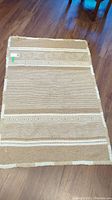 Full view of beige and off-white wool rug on hardwood floor showing two-color patterned stripes and fringed edges