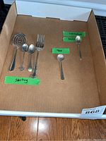 Photo of all flatware items laid out on cardboard with green tapes showing markings and brand notes