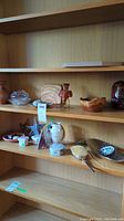 Photo of wooden shelf with various decorative items including star sun catchers, porcelain boxes, wooden bird candle holder, hair brush, and small vases.