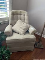 Beige swivel armchair with matching pillow, showing front and side angles, near window and floor lamp.