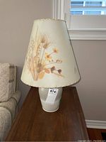 Full front view of the table lamp on wooden table, depicting ceramic base and floral dried flowers lampshade.