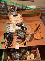 Photo of the Craftsman drill with cord, yellow portable flood light, Teco Master soldering kit in white case, wooden hand saw, clamps, and other hardware items scattered on wooden surface.