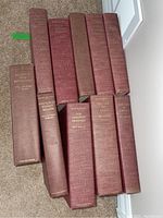 Top-down photo showing all ten hardcover red cloth bound books arranged on carpet, titles visible on spines.