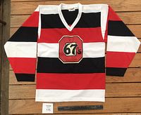 Front view of the Ottawa 67's hockey sweater showing the red and black striped pattern and crest.