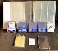 Photo showing open binder with nine-pocket pages and various sealed card holder packs and card sleeves in front.
