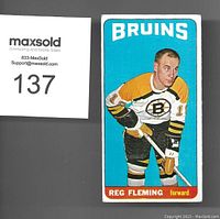 Front of the 1964-65 Topps Tall Boy Reg Fleming hockey card showing player in Boston Bruins uniform with blue background and identification text.