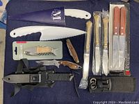 Assorted kitchen knives including serrated bread knives, corkscrew bottle openers, and a black handled knife with sheath.