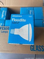 Close-up of a single blue individual box labeled 'Sylvania Floodlite' with a bulb illustration, indicating floodlight bulb for indoor and outdoor use.