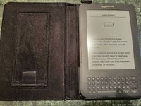 Amazon Kindle device inside open black Speck protective case showing screen with 'Empty Battery' error message and physical keyboard.