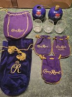 Photo showing all items in the lot: two large Crown Royal bags, three smaller bags, three shot glasses, and two metal ornaments shaped like Crown Royal bags.