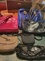 Eight handbags in various colors and designs laid out together showing full lot contents