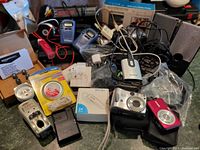 Overview of all items in the electronics lot including cameras, radios, chargers, wires, and batteries on a countertop.