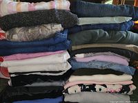 Stack of 31 folded women's size large clothing items including various pants, tops, and sweaters in assorted colors and fabrics.