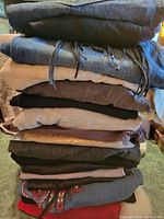 Stack of various folded ladies' size large clothing pieces in multiple fabrics and colors including denim, black, beige, brown, and red with visible embroidery on one item