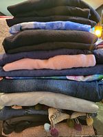 Stack of folded clothing items showing variety of colors and materials including knit, denim, and cotton fabrics.