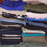Stack of ladies' clothing including pants, skirts, and tops in various colors and fabrics.