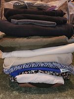 Stack of 14 folded clothing items in various colors including black, gray, olive green, cream, white, blue, and floral patterns
