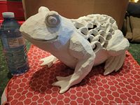Front-side angle of large white resin frog next to water bottle for scale