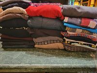 Photo showing multiple folded men's tops and pants in assorted colors and patterns stacked in three piles.