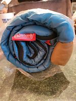 Rolled and secured blue Coleman sleeping bag showing the Coleman red tag and black strap.