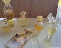 Six Nina Ricci perfume bottles on a white surface, various shapes and sizes, yellow perfume liquid inside, some with decorative caps such as silver dove or gold ribbed.