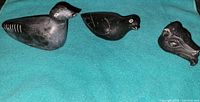 Photo showing two soapstone loons and one reptilian head on teal cloth background.
