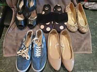 Overview image showing all five pairs of footwear laid out on a brown towel: black and beige heels, black pom-pom slippers, tan flats, denim sneakers.