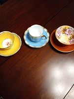 Photo showing the three teacups and saucers on a wooden table, displaying the yellow, blue, and floral sets