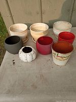 8 various small flower pots arranged on a surface outside near a cabinet, showing different colors and styles.