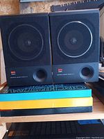 Pair of black Aiwa SC-47 bookshelf speakers side by side on a shelf with books beneath them, showing fronts including bass reflex ports.