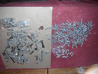 Wide view showing assortment of bolts, nuts, washers, some plastic anchors, spread on a surface.