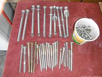 Top down view of assortment of bolts laid out on a surface showing various sizes, primarily lag bolts and carriage bolts, with a bucket of smaller bolts and screws.