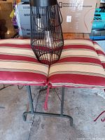 Patio chair cushion in striped beige, red, and white fabric with patio lantern placed on top.