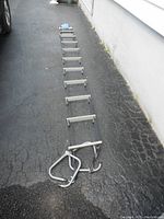 Full length of metal rung emergency escape ladder laid out on asphalt, view showing metal rungs and blue securing strap with handle.