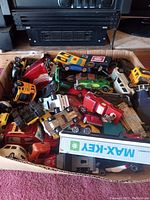 Image showing a box filled with numerous toy vehicles including cars, trucks, and construction equipment, predominantly metal with some plastic parts, various colors and models.