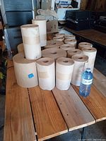 Sixteen new brown paper towel rolls of assorted sizes arranged on a wooden table with a water bottle for scale.