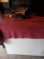 Full view of the rotisserie kits components including motor, brackets, pronged forks, and rod on red cloth with box