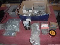 Wide view of various screws, nuts, bolts, and fasteners in boxes and plastic bags on a table.