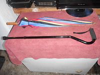 Photo showing the multi-colored umbrella and the black adjustable walking cane on a pink cloth surface.