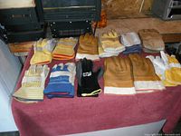 All 12 pairs of men's work gloves laid out on a red towel, showing variety in style and colors such as yellow, tan, white, blue, and black. Gloves appear mostly new, size large and extra-large.