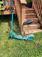 Blue Razor E200 electric scooter with padded black seat. Scooter is positioned outdoors on grass beside wooden steps.