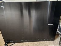 Black Samsung wireless subwoofer, rectangular with Samsung logo visible, placed on carpet