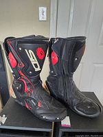 Pair of black Sidi motorcycle boots with red protective accents, positioned upright side by side.