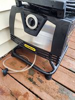Close-up of Stanley power washer showing brand logo, base frame, and water hose connection area. Signs of wear and outdoor use visible.