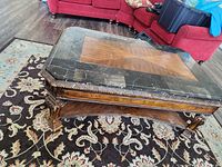 Photo of a rectangular coffee table with a wood center panel and black marble top with carved wooden legs.