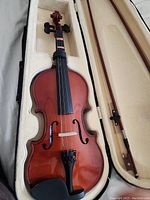 Violin laid in cream padded hard case with bow beside it