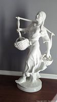 Full side view showing the entire figure with baskets and yoke against a grey wall.