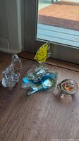 Hand blown glass fish, rabbit, and seal figurines with colorful accents displayed on a wooden floor near a door.